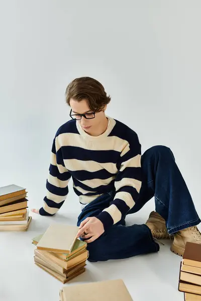 A young man in a striped sweater engages deeply with textbooks while sitting on the floor. — Stock Photo