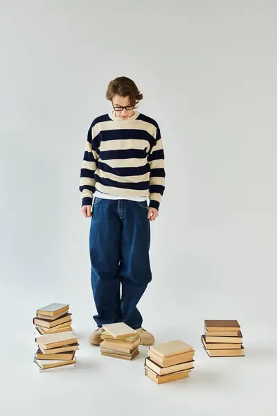 Young man in a striped sweater explores his college years surrounded by books in a warm studio. — Stock Photo