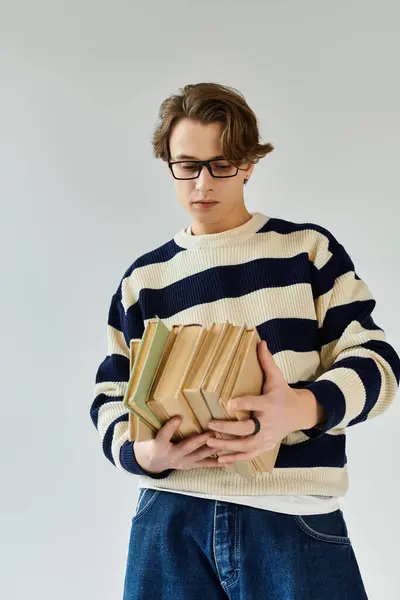A young man in a striped sweater stands thoughtfully, holding a stack of books in a studio. — Stock Photo