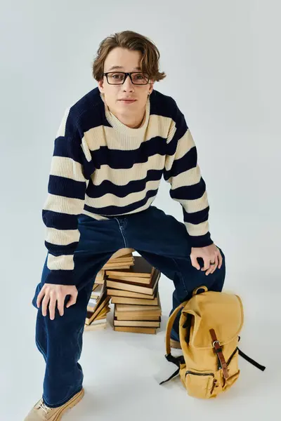 A young man sits confidently among stacks of books, wearing a striped sweater and ready for college. — Stock Photo