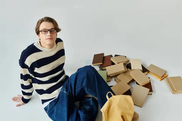 A stylish young man sits casually surrounded by a scatter of books, embodying student life. — Stock Photo