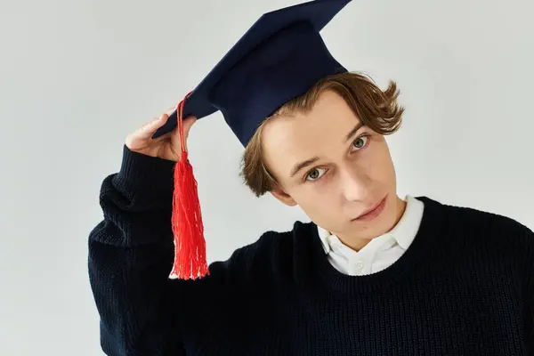 Um jovem estudante bonito ajusta seu boné de formatura, mostrando sua realização em um estúdio. — Stock Photo