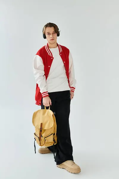 A handsome young man stands confidently in a studio, wearing a stylish bomber jacket and headphones. — Stock Photo