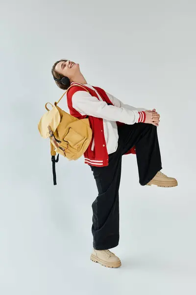 Young man dressed in a bomber jacket and backpack confidently poses in a studio space. — Stock Photo