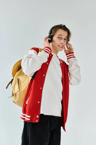 Young man with a backpack listens to music while posing in a bright studio space. — Stock Photo