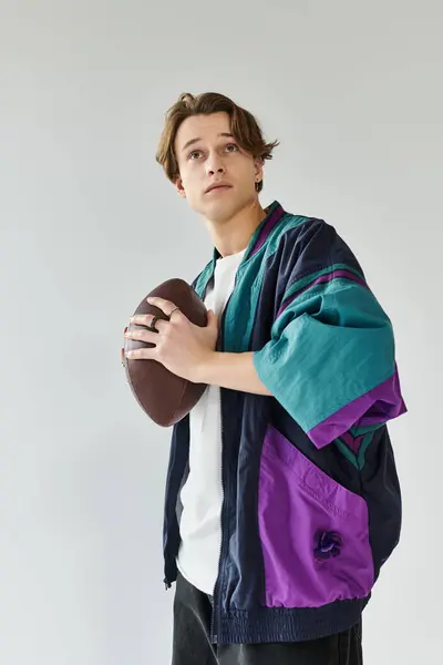 A handsome young man dressed in a fashionable bomber jacket poses with a football in a studio space. — Stock Photo