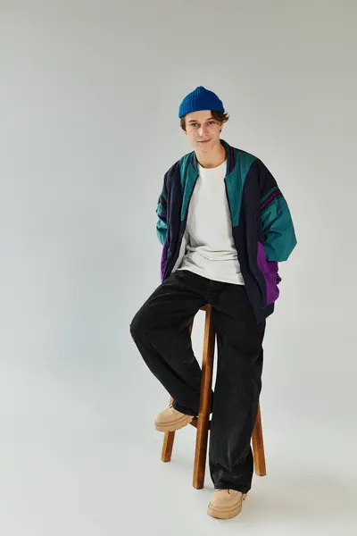 A handsome young man sits on a stool, showcasing his stylish bomber jacket in a studio. — Stock Photo