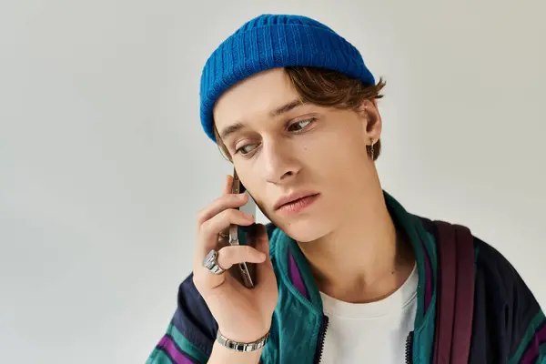 A young man wearing a trendy bomber jacket speaks on his phone in a creative studio space. — Stock Photo