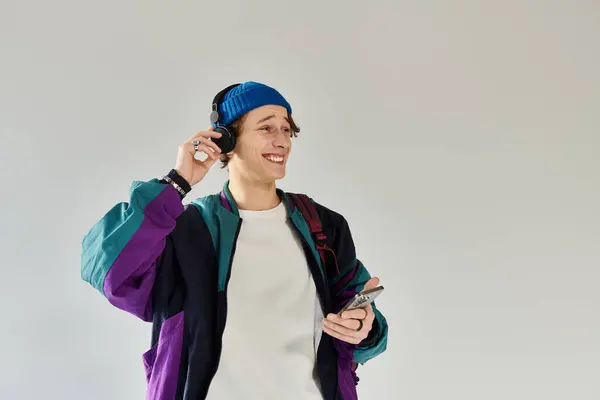 A young man wearing a colorful bomber jacket smiles while listening to music in a studio. — Stock Photo