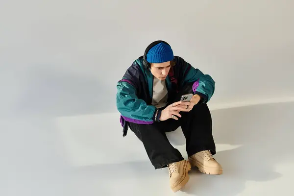 A young man sits on the floor, focused on his phone while wearing a trendy bomber jacket. — Stock Photo