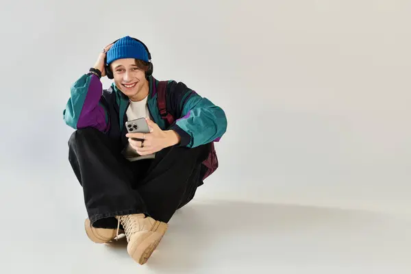 A young man in a bomber jacket smiles while casually using his phone in a studio. — Stock Photo