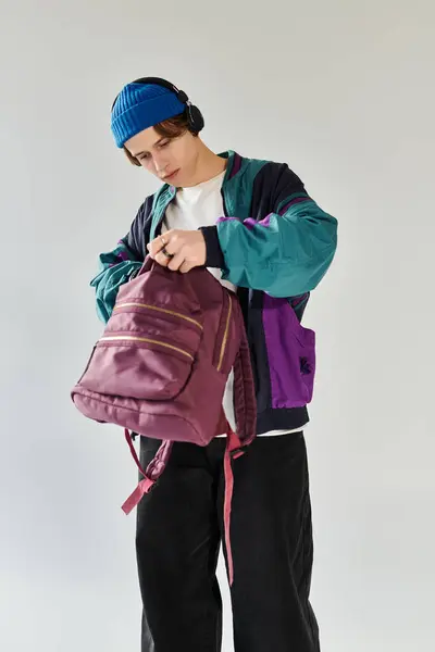 Un jeune homme vêtu d'une veste bombardier tendance ajuste son sac à dos dans un studio. — Photo de stock