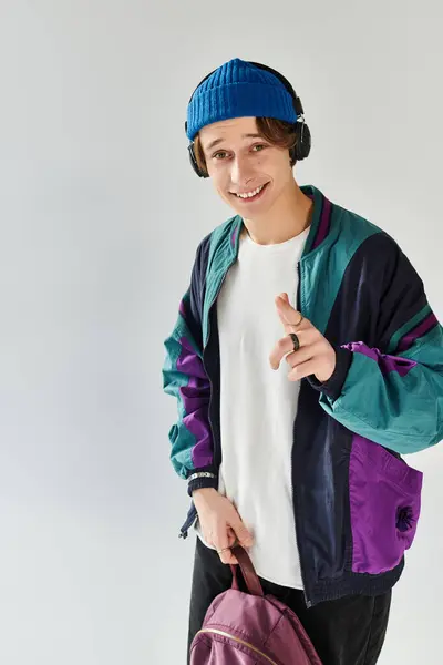 A handsome young man wears a stylish bomber jacket and beanie while smiling in a bright studio. — Stock Photo