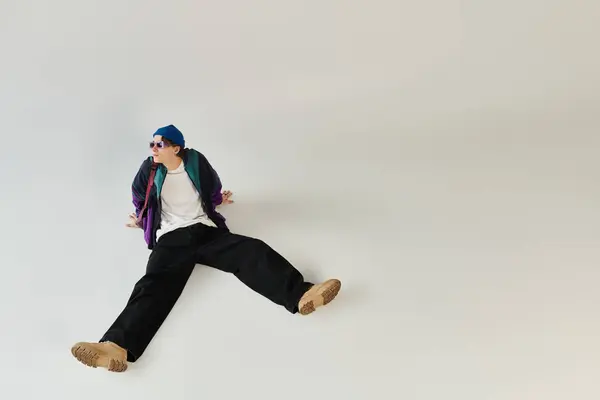 A young man dressed in a bomber jacket relaxes on the studio floor, showcasing his trendy style. — Stock Photo