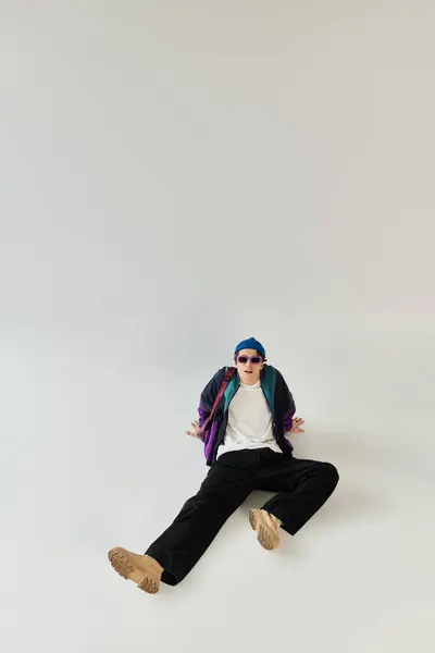 A young man showcases his trendy bomber jacket while sitting casually in a stylish studio. — Stock Photo