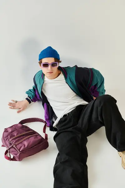 A young man wearing a bomber jacket and beanie lounges in a creative studio environment. — Stock Photo