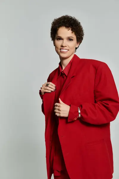 Charming woman dressed in a bold red outfit stands confidently against a neutral backdrop, smiling. — Stock Photo