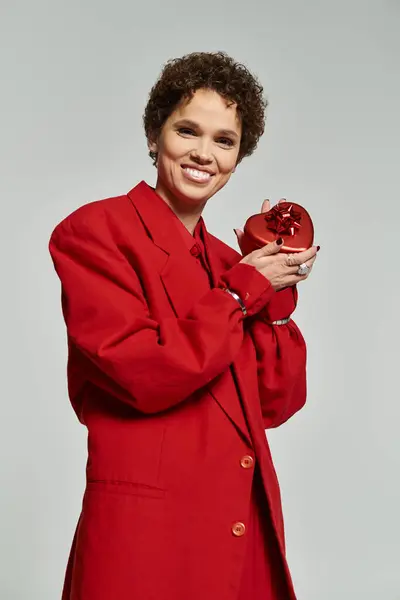 Brightly dressed in a striking red outfit, a young woman holds an artistic object with a warm smile. — Stock Photo