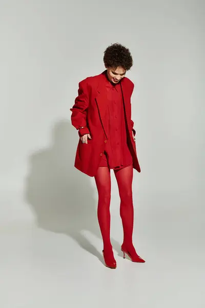 Young woman stylishly dressed in a red ensemble, confidently posing against a neutral background. — Stock Photo