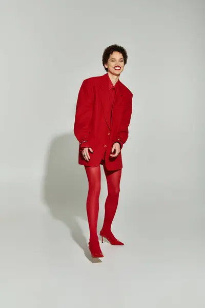 A confident young woman in a striking all red outfit radiates joy in a modern studio. — Stock Photo