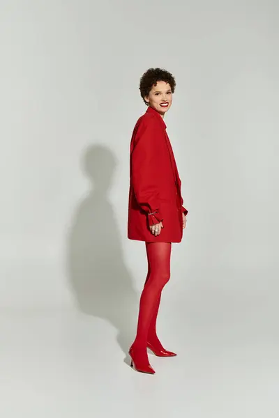 A young woman in a striking red outfit poses confidently against a plain backdrop. — Stock Photo