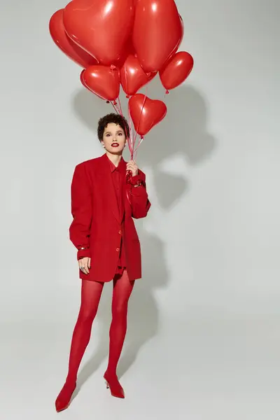 Une femme élégante pose avec confiance avec des ballons rouge vif, exhibant de façon ludique dans un studio. — Photo de stock