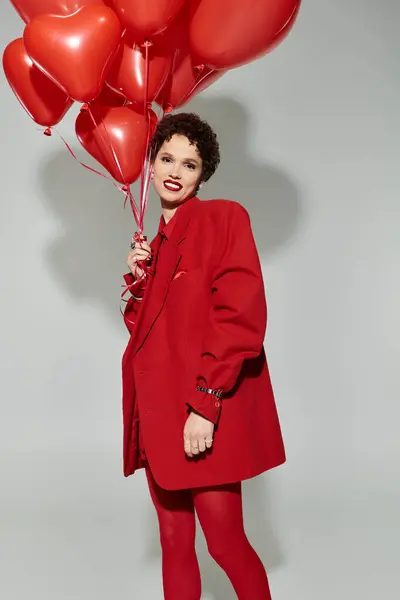 Une jeune belle femme rayonne de joie tout en tenant des ballons en forme de cœur, vêtus de rouge frappant. — Photo de stock