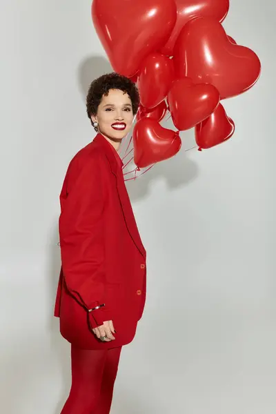 Une femme élégante en rouge tient joyeusement des ballons en forme de cœur. — Photo de stock