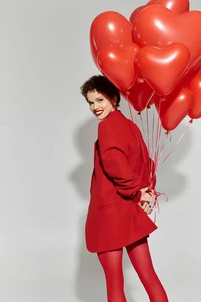 Junge Frau genießt einen verspielten Moment mit herzförmigen Luftballons in lebendiger Kleidung. — Stockfoto