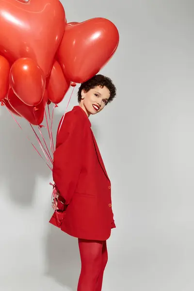 Une jeune femme vêtue de rouge tient des ballons en forme de cœur, rayonnant de joie et de confiance. — Photo de stock