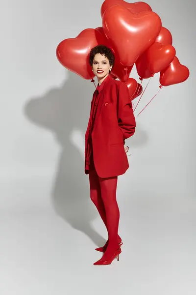 A stylish young woman poses gracefully, holding bright heart shaped balloons in vibrant red. — Stock Photo