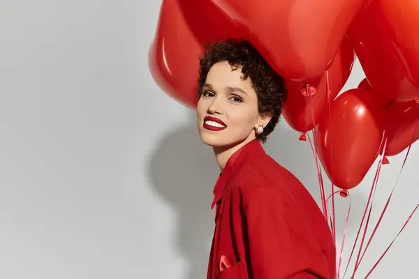 Une jeune femme élégante rayonne de joie tout en tenant des ballons rouges vibrants, embrassant le moment. — Photo de stock