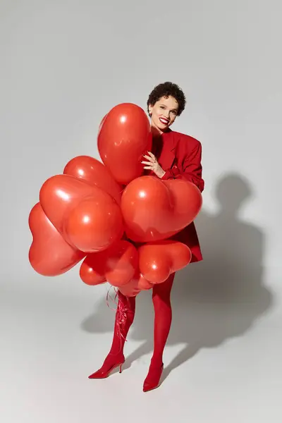 Une jeune femme en rouge embrasse joyeusement les ballons en forme de cœur. — Photo de stock
