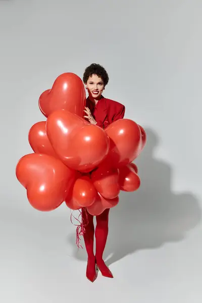 A young woman in vibrant red clothing holds heart shaped balloons, radiating joy. — Stock Photo