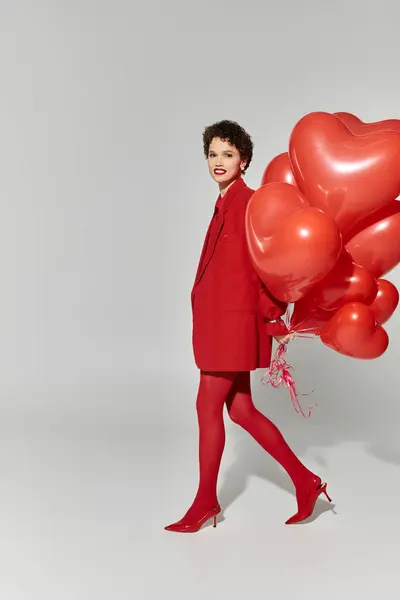 Eine junge Frau im knallroten Outfit geht anmutig mit herzförmigen Luftballons. — Stockfoto