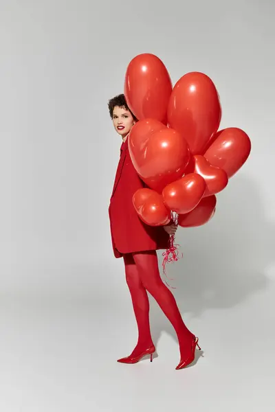 Une jeune femme vêtue de rouge vif tient une grappe de ballons lumineux, rayonnant de joie. — Photo de stock