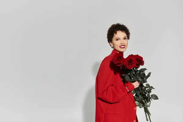 A stylish young woman dressed in red holds a bouquet of fresh roses, exuding confidence and charm. — Stock Photo