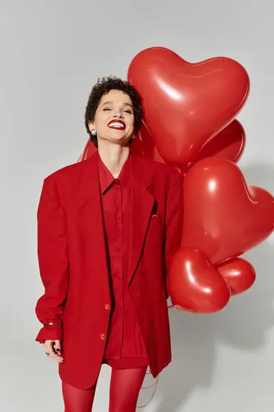 Une jeune femme vêtue de rouge vif respire le bonheur tout en tenant des ballons en forme de cœur. — Photo de stock