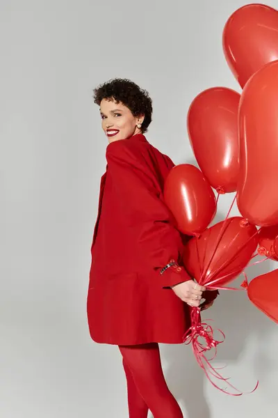 Une jeune femme en tenue rouge saisissante tient une grappe de ballons rouges, exsudant le bonheur. — Photo de stock