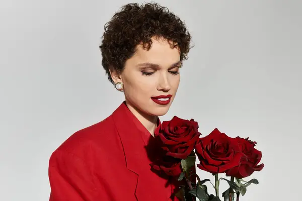 A young beautiful woman enjoys a moment holding red roses, showcasing vibrant fashion and elegance. — Stock Photo