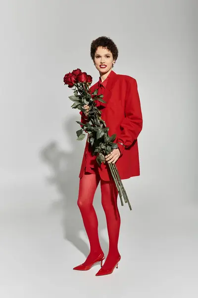 A young woman in a red outfit holds roses and exudes elegance. — Stock Photo