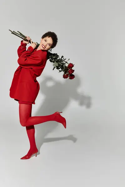 A stylish young woman smiles, playfully holding red roses and showing off her outfit. — Stock Photo