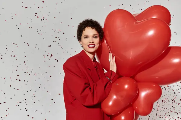 Eine stylische junge Frau umarmt herzförmige Luftballons und strahlt Freude bei einem festlichen Ereignis aus. — Stockfoto