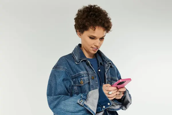 A young woman with curly hair smiles as she texts on her smartphone, showcasing her fashion sense. — Stock Photo