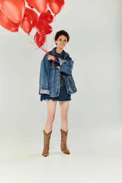 Femme lumineuse et joyeuse aux cheveux bouclés s'amuse tout en tenant des ballons rouges dans un cadre ludique. — Photo de stock