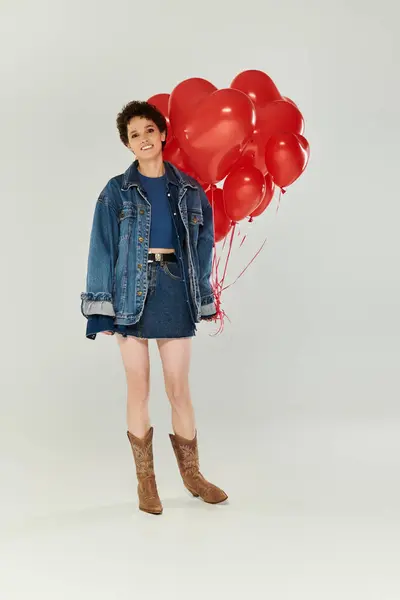 Une jeune femme sourit vivement, tenant des ballons rouges vibrants dans sa tenue élégante. — Photo de stock