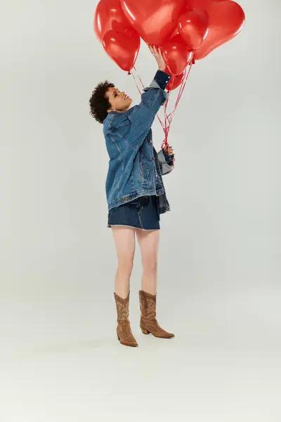 Une jeune femme en denim tient joyeusement des ballons colorés en forme de cœur. — Photo de stock