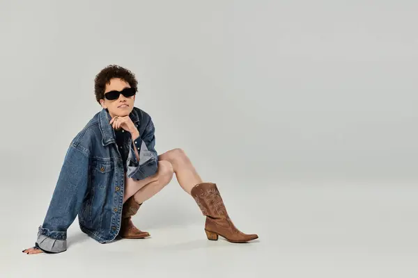 Mujer joven muestra su estilo de moda mientras se sienta cómodamente en un traje elegante y botas. - foto de stock