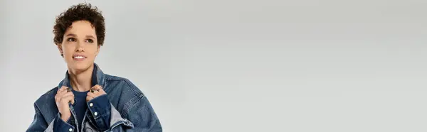 Confident young woman smiles in a trendy denim jacket against a light background. — Stock Photo