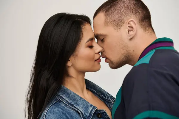 A beautiful couple dressed in trendy outfits shares a loving kiss in a studio. — Stock Photo